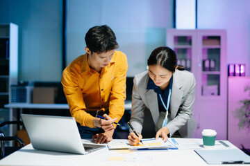 Obraz premium Asian business colleagues collaborating in modern office, discussing documents and strategy, teamwork, consulting and professional corporate workflow.