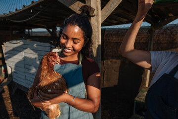 Young farmer woman holding hen in chicken coop