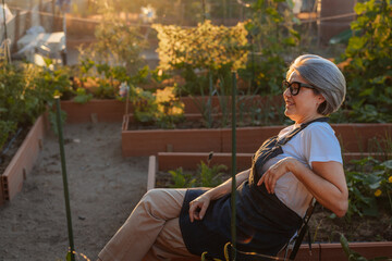 Senior woman gardener relaxing in her urban garden at sunset