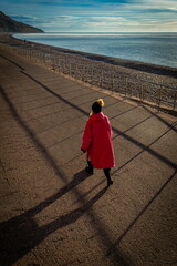 woman in red coat walking on the beach in Seaton, Devon