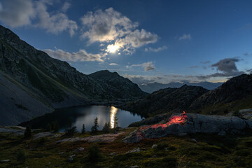 Lone hiker with a red headlamp during a moonlit bivouac at Lacs de Vens, Mercantour National Park. © Alevsian