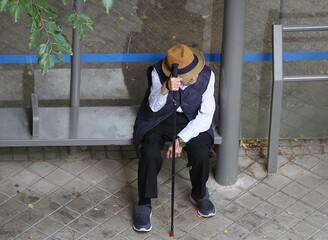 abuelo viejo con bast&oacute;n y sombrero esperando sentado en parada de bus al autob&uacute;s