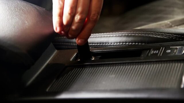 Detail shot of human hand connecting black USB cable into auxiliary power outlet of vehicle center console. Focus on connection process of charger.
