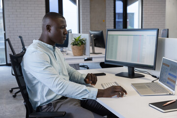 African American man working on spreadsheet on external monitor at modern office, copy space