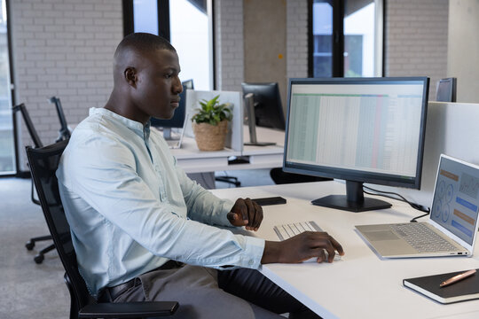 African American man working on spreadsheet on external monitor at modern office, copy space