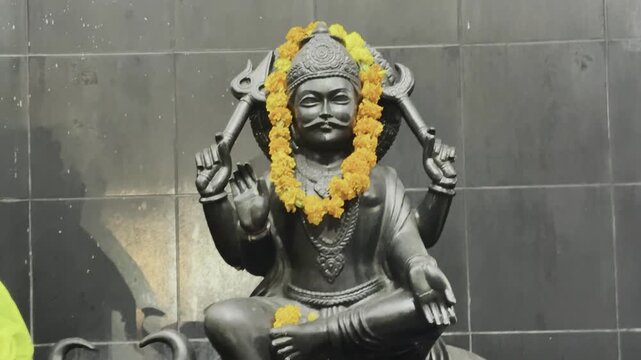 Black stone idol of Lord Shani Dev adorned with yellow marigold garlands, symbolizing devotion, planetary worship, and divine justice.