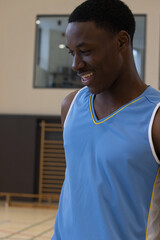 Fototapeta premium African American adult male wearing basketball jersey standing smiling in gym with stall bars