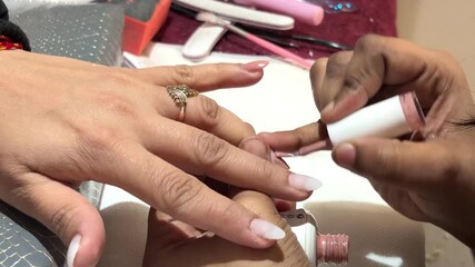 Close-up of a professional nail care procedure where a beautician applies nail polish or gel coating to a client’s fingernails. The image captures precision hand movements, glossy nail 