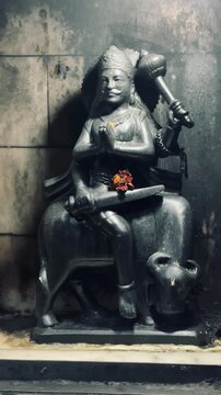 Lord Shani Dev seated in a temple shrine, worshipped with a lit oil lamp symbolizing justice, discipline, and karmic balance in Hindu devotion