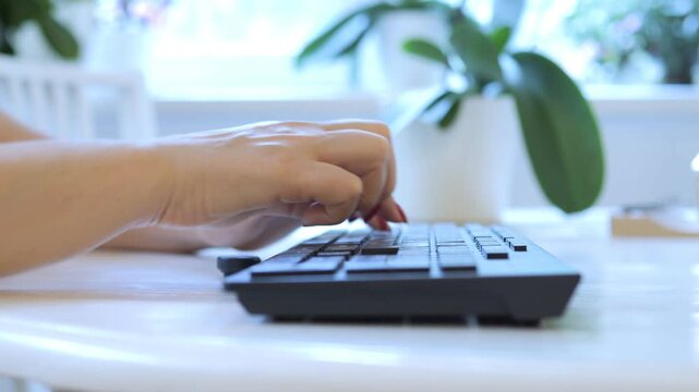 Person is typing on a keyboard. The keyboard is black and has a white keypad. The person is using the space bar and the shift key