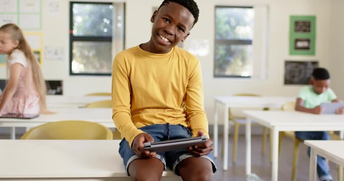 Diverse classmates, African American male youth tapping tablet, glancing up and laughing in class