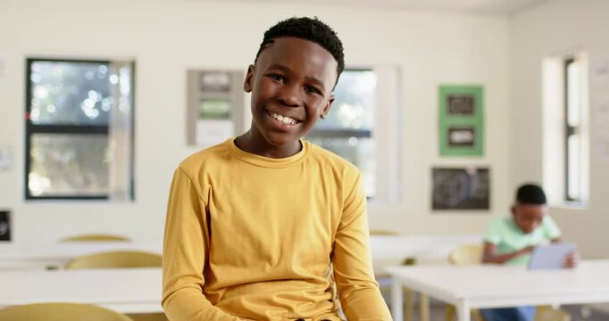 African American male youth student tapping tablet in classroom, viewing funny clip and laughing
