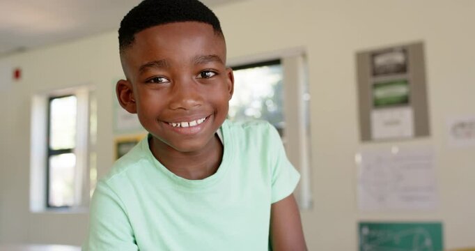 African American boy looking up from paper, responding to camera and smiling at classroom table