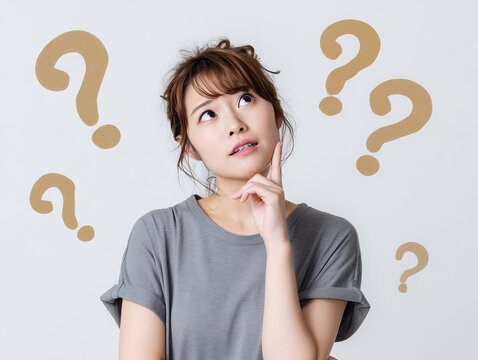 疑問符に囲まれ考え込む表情を見せる若い女性の悩みシーン