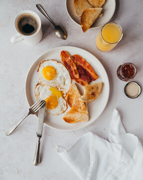 Overhead of plate of bacon, eggs, toast with drinks for breakfast.