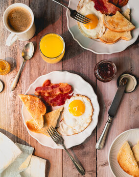 Top view of plates of bacon, eggs, toast with drinks for breakfast.