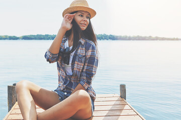 Summer, boardwalk and woman by lake for holiday, vacation and relax on weekend getaway with style. Thinking, fashion and girl sitting by water, river and outdoor for travel, break and trip in nature