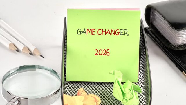 A light green note transforms from cryptic symbols to readable text, ultimately revealing plans for a game changer in 2026. Pencils, a magnifying glass, and crumpled notes surround it