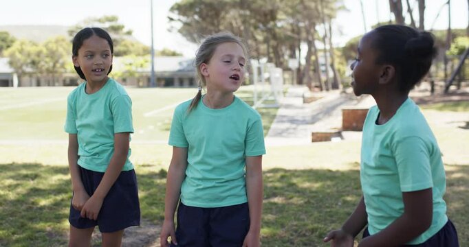 Three preteen girls in teal shirts and dark shorts talking by goalpost, center girl starting play