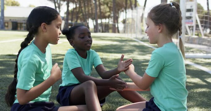 Diverse school-age girls playing clap game on field, center girl starting claps in light green tees