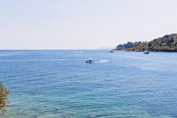 Obraz premium Speedboat cruising across turquoise sea with sailboats and green coastline in distance
