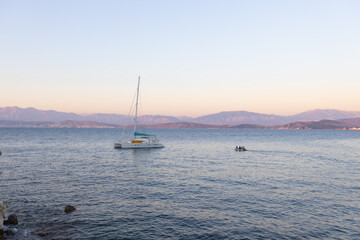 Fototapeta premium Tranquil sailboat anchored in serene bay at sunset with distant mountains
