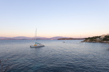 Fototapeta premium Tranquil sailboat anchored in serene bay at sunset with distant mountains