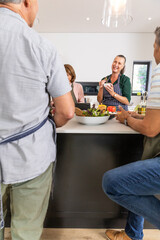 Senior friends in aprons chopping herbs and tossing greens with cherry tomatoes at kitchen island © wavebreak3