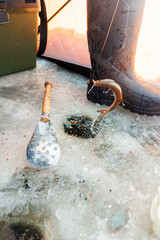 A small fish flips from a drilled ice hole beside a wet boot, water droplets freeze midair, an ice...