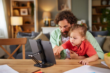 A father and his young child enjoy quality time at home, exploring a device together at the kitchen table. Their expressions are happy as they engage with each other.