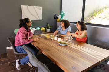 Diverse friends chatting at dining table with snack bowls, pouring water from clear pitcher