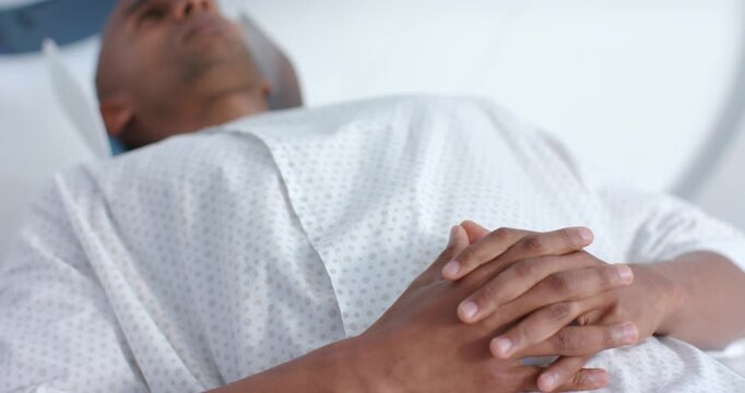African American man lying on hospital gown clasping hands while table moving into scanner for MRI