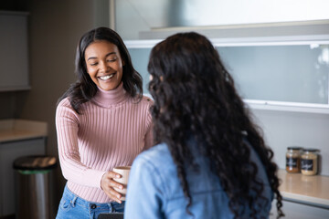 Diverse female coworkers exchanging coffee mug in office kitchenette with jars, trash bin