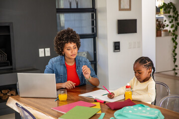 African american mother and daughter studying at home on table with laptop, workbook, pencil