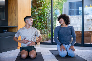 Diverse male friends kneeling on mats practicing breathing with fitness trackers in living room