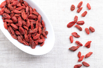Goji berries, dried fruits in white bowl on linen. Also Chinese wolfberry, red medlar, and matrimony vine. Bright, orange-red, sweet fruits of Lycium barbarum, native to China and across Asia. Photo