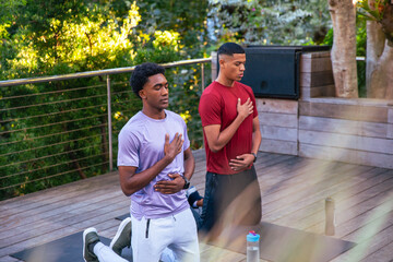 Diverse male friends kneeling on exercise mats on deck by metal railing with water bottles