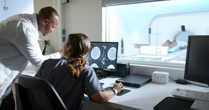 Staff at console reviewing CTs while watching patient as table entering gantry, copy space