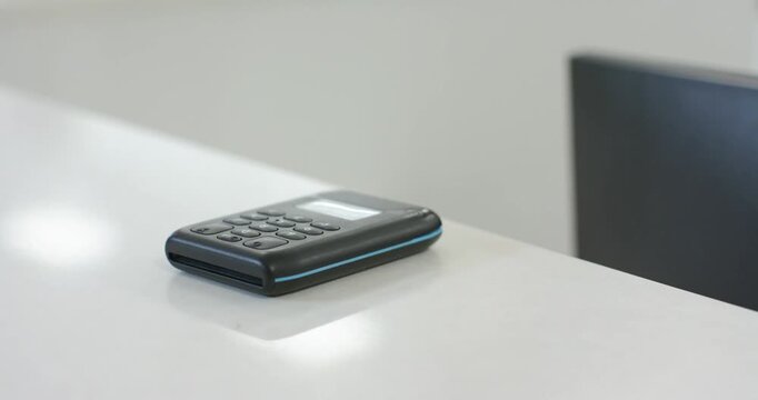 Camera is dollying in, highlighting black keypad device sitting on white desk and reflections