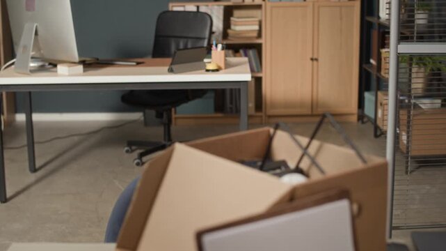 Rack focus no people shot of cardboard resignation box with I quit my job sign left on desk in empty modern office workspace