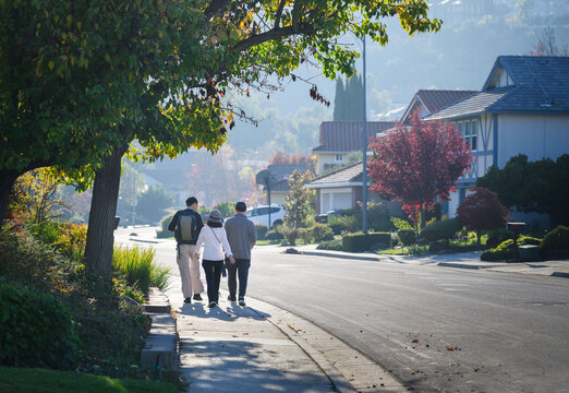 Three people walking on the pedestrian footpath in autumn. Walkable city in California. USA.
