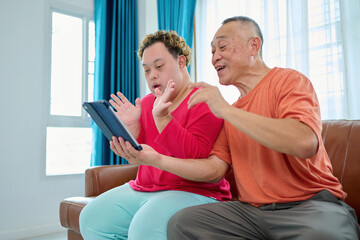 A man with down syndrome and senior man sharing an excited moment together while looking at a tablet on a sofa © offsuperphoto