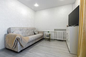 Bright living room interior with beige sofa and TV on white cabinet