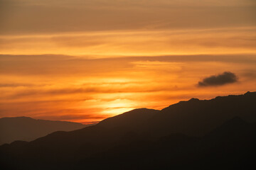 Beautiful bright orange sunset sky with clouds over the mountains silhouette. 