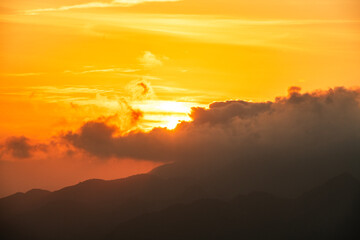 Beautiful bright orange sunset sky with clouds over the mountains silhouette. 