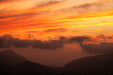 Beautiful bright orange sunset sky with clouds over the mountains silhouette. 