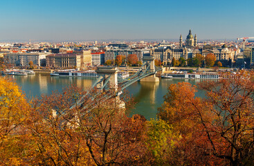 Obraz premium Budapest cityscape, panoramic view of city and Danube River with Chain bridge and beautiful architecture in autumn season, trees, branches and yellow leaves in foreground