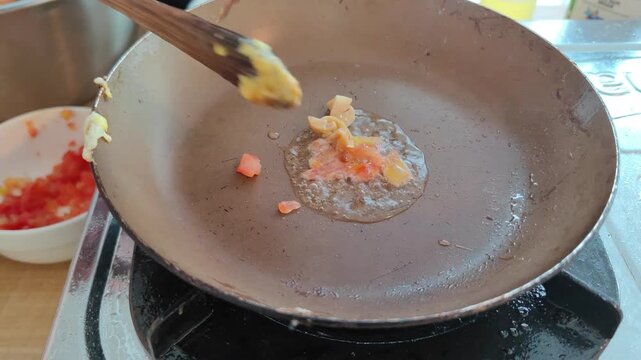 Close-up video of small diced ingredients being stir-fried in a pan using a wooden spatula. Cooking process on a stovetop with visible oil and fresh chopped vegetables in the background. Perfect for c