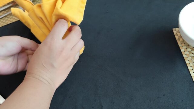 Close-up shot of hands neatly folding a bright yellow t-shirt on a black table surface. The video shows an organized clothing folding process, ideal for concepts of laundry, home organization, minimal