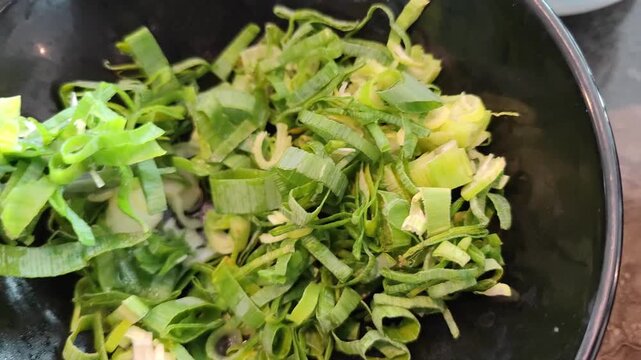Close-up video of freshly chopped green onions in a bowl being picked up with metal tongs. Vibrant green color and fresh texture highlight healthy cooking ingredients and food preparation process. Per